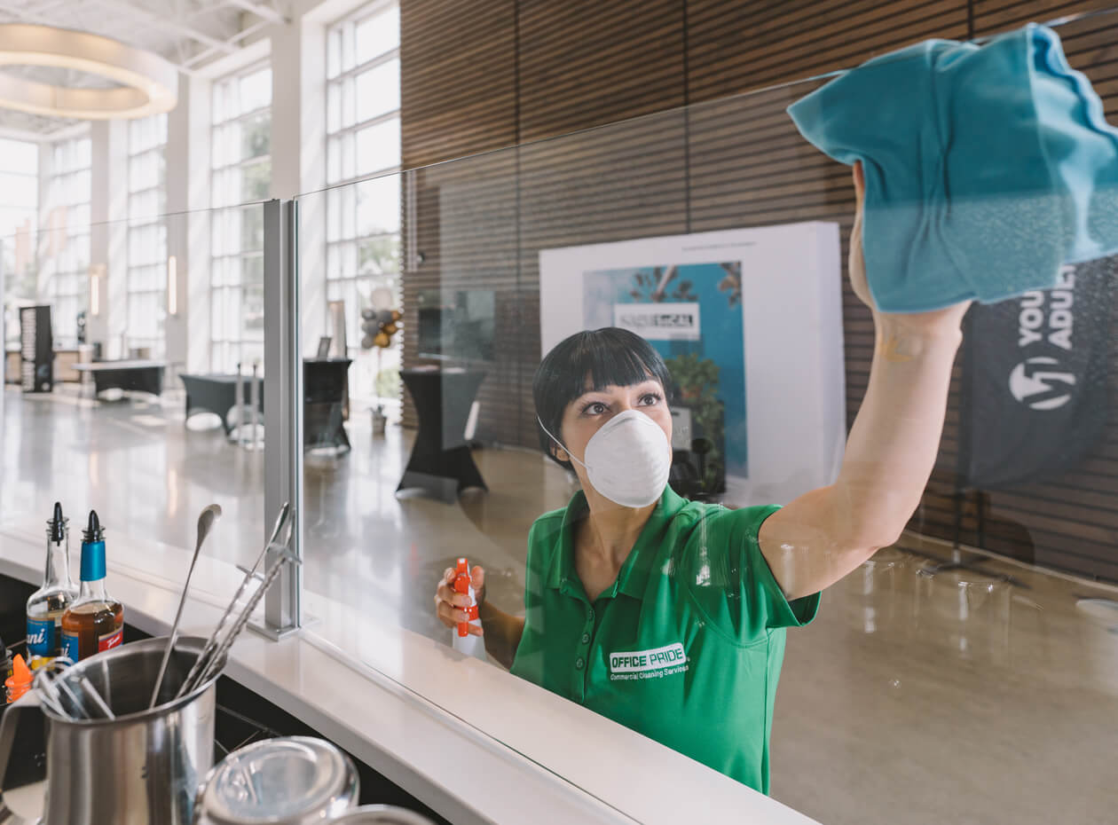 commercial cleaner wiping down glass divider between restaurant and public walk way inside office building