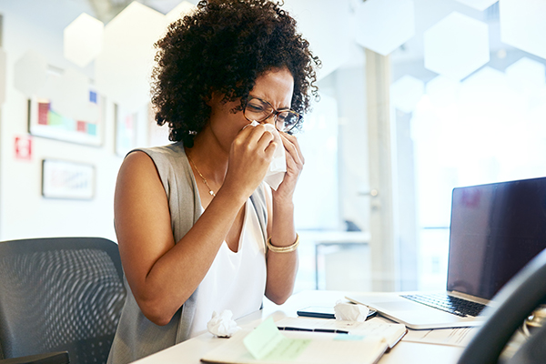 Sick employees blowing her nose at desk
