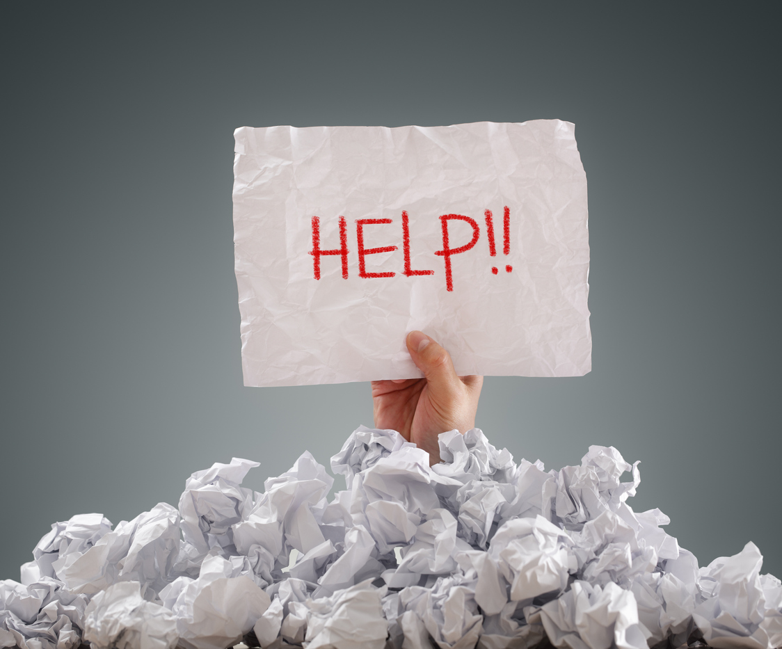 pile of paper balls with a hand extending out holding a sign that reads help
