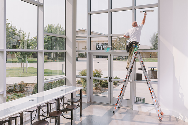 Professional Commercial cleaner on a ladder cleaning the window above the entrance doors of a corporate building during the afternoon