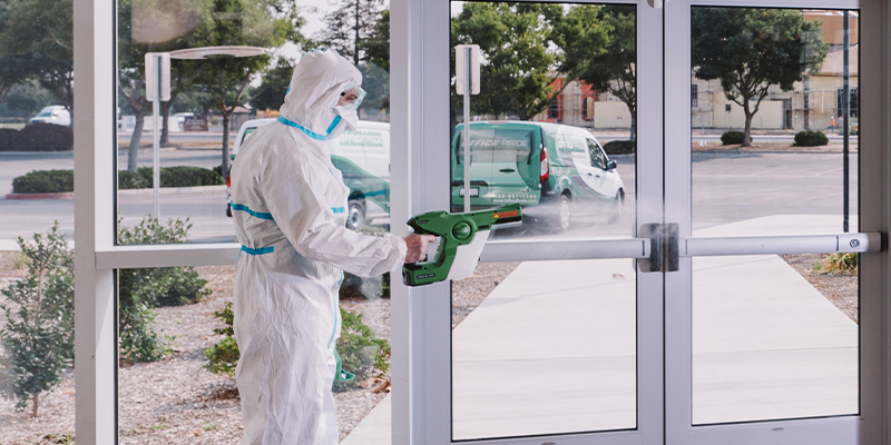 Commercial cleaning professional in full cleaning suit using touch-less techniques to provide sanitation services in a corporate building lobby