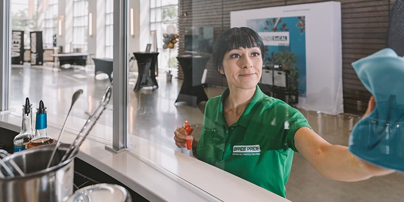 Professional Cleaner wiping the glass meant to separate the public from the food prep area inside a company cafeteria
