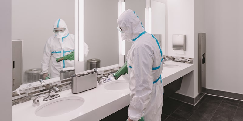Professional commercial cleaner using a electrostatic sprayers inside a restroom of a workplace